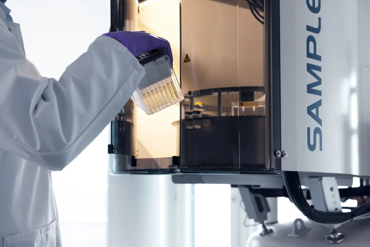 A gloved laboratory scientist loading a rack of sample tubes into an NMR spectrometer's sample changer